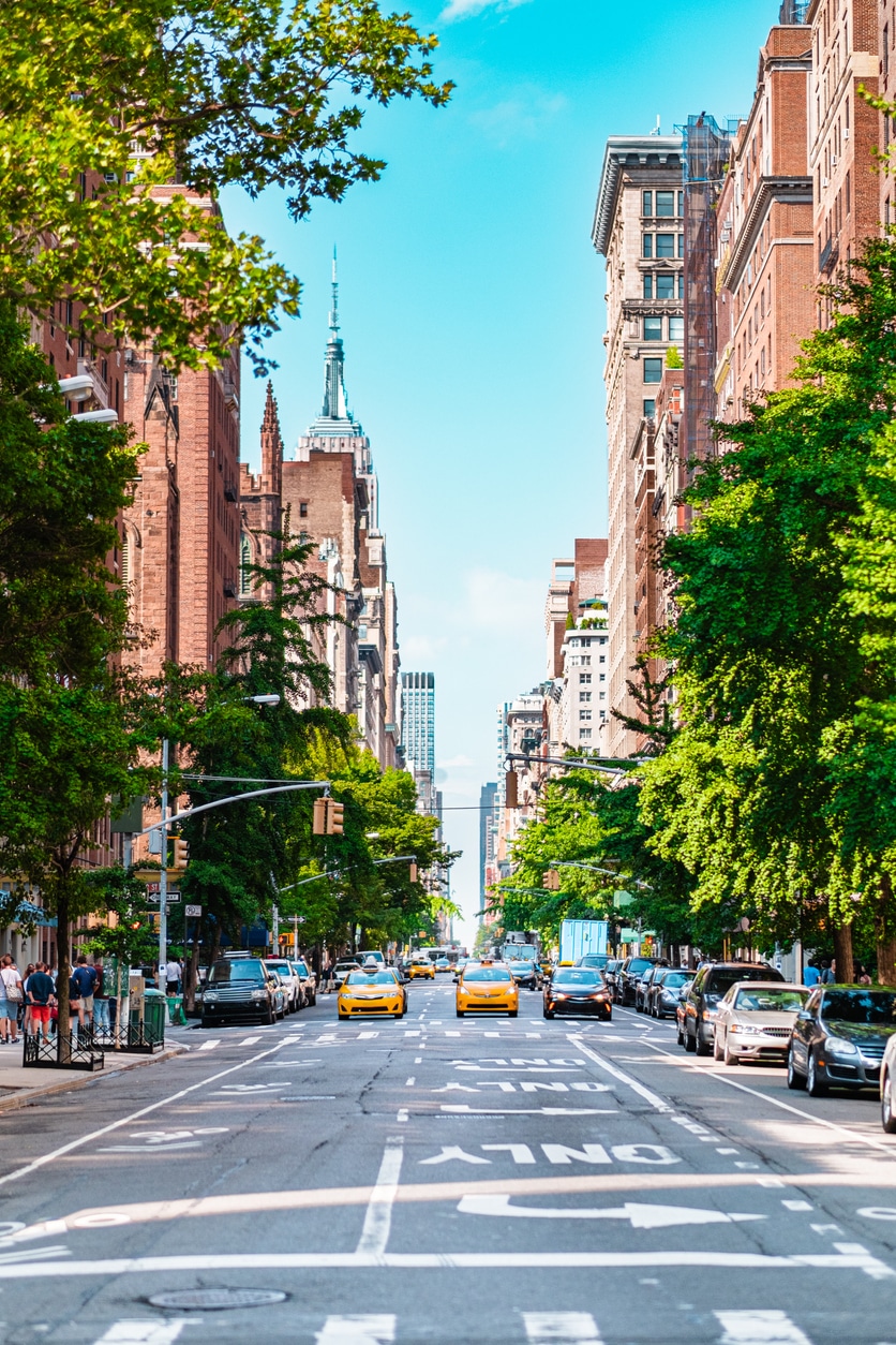 Bustling Urban Scene in New York City Featuring Iconic Yellow Taxis and Towering Skyscrapers on a Bright Sunny Day with Vibrant Green Trees Flanking the Streets Under a Clear Blue Sky
